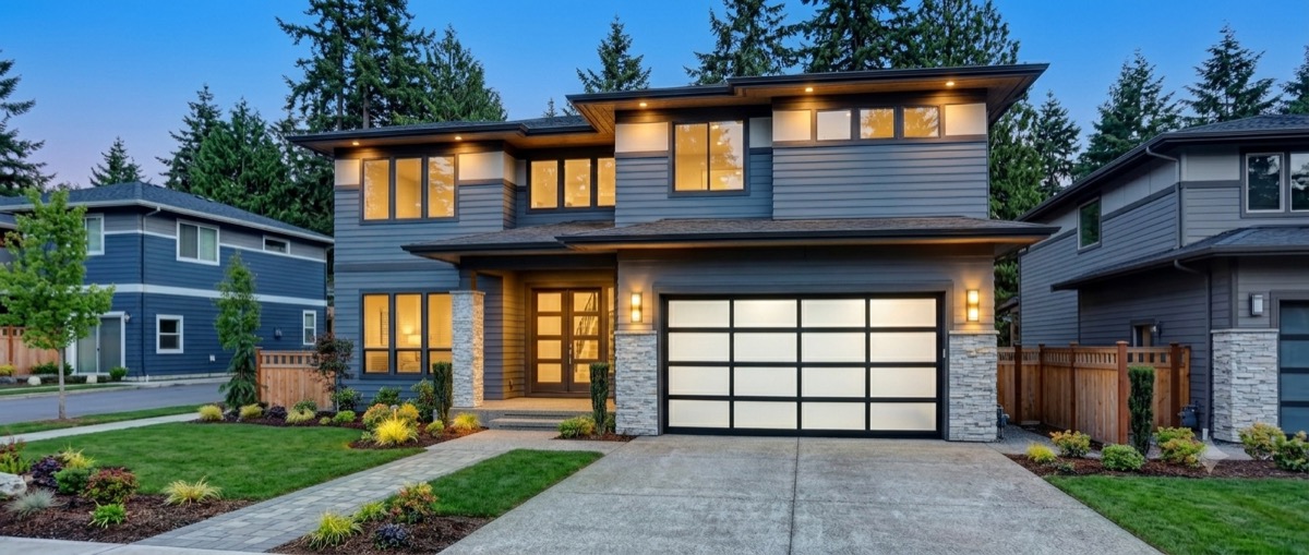 A modern two-story home at dusk with an illuminated garage — Garage Door Guide, Portland OR & Vancouver WA